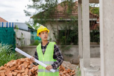 Mühendis konsepti açık yeşil gömlekli genç mühendis ve binanın ikinci katını gösteren sarı kasklı adam..