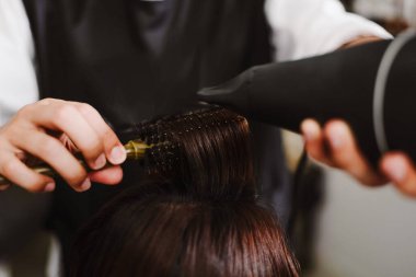 Kuaför salonu konsepti bir tutam saç almak için tarak kullanan bir erkek kuaför ve saç kurutma makinesini kurulama ve düzeltme için kullanıyor.