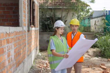 Mühendislik konsepti. Başlıklı ve maskeli iki bina yöneticisi binanın yanında duruyor ve binanın diyagramına bakıyor..