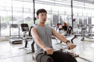 Egzersiz konsepti. Egzersiz kulübündeki kaslı adam dikkatini koltuğun yuvarlanma makinesine vererek yatay olarak kendine doğru çekiyor..