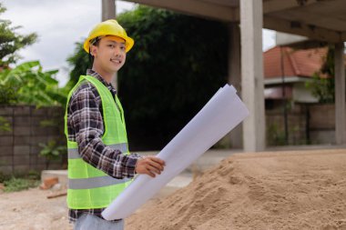 Mühendis konsepti Sert sarı şapka giyen, koyu renkli ekose bluz giyen ve inşaat binasına bakan inşaat manipülatörü.