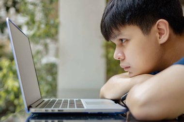 Çevrimiçi konsept üzerinde çalışan genç çocuk çenesini kollarına dayayıp dizüstü bilgisayara bakıyor, işine devam etmek için hiçbir fikri yok, bu da onu şu anda çalışmaktan bezdiriyor..