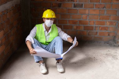 Mühendis konsepti. Erkek inşaatçı, binanın zeminine tüneyen, bina diyagramını açan ve gözlerini binanın duvarına dikmiş..