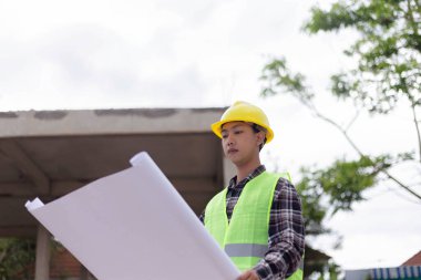 Mühendis konsepti Sert sarı şapka giyen, koyu renkli ekose bluz giyen ve inşaat binasına bakan inşaat manipülatörü.