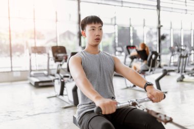 Egzersiz konsepti. Egzersiz kulübündeki kaslı adam dikkatini koltuğun yuvarlanma makinesine vererek yatay olarak kendine doğru çekiyor..