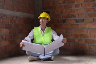 Mühendis konsepti. Erkek müteahhit yere oturup bugünkü çalışma planını ciddi bir suratla okuyor..