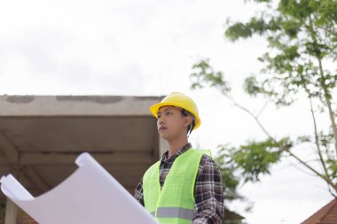 Mühendis konsepti Sert sarı şapka giyen, koyu renkli ekose bluz giyen ve inşaat binasına bakan inşaat manipülatörü.