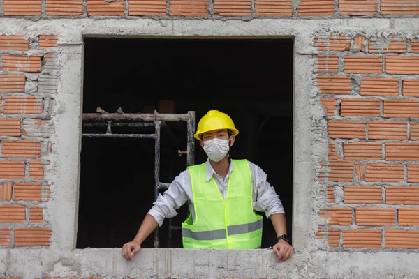 engineer concept The building worker who puts on safety devices such as a vibrant yellow hat and a white mask attempting to gaze at the scene out of the window.