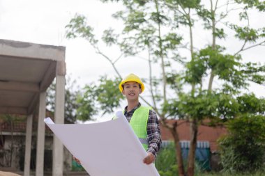 Mühendis konsepti Sert sarı şapka giyen, koyu renkli ekose bluz giyen ve inşaat binasına bakan inşaat manipülatörü.