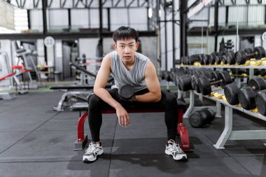 Spor konsepti. Gri spor bluzlu, siyah pantolonlu kaslı adam. Sağ kolunda konsantrasyon kıvrımı yaparak halterle çalışan siyah bir akıllı adam..