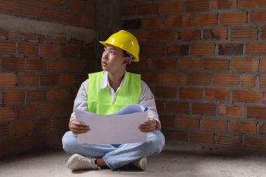 Mühendis konsepti. Erkek müteahhit yere oturup bugünkü çalışma planını ciddi bir suratla okuyor..