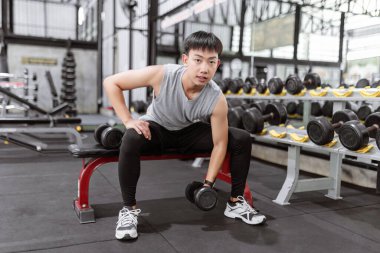 Spor konsepti. Spor adamı sol eliyle dambılı kaldırırken diğer dambıl da sağ tarafındaki bankta..