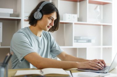 Uzaktan eğitim kavramı, genç çocuk derste kulaklık takıyor ve Skype 'ta sohbet yazıyor..