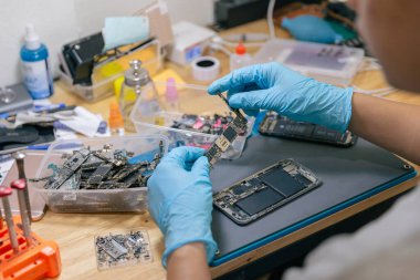 Telefon tamir konsepti. Elektronik kısmı seçen bir tamirci. Masadaki aletlerle cep telefonuyla monte etmek için..