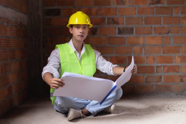 Mühendis konsepti. Erkek müteahhit yere oturup bugünkü çalışma planını ciddi bir suratla okuyor..