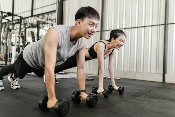 exercise concept The female and male members of the gym doing the basic renegade row posture with dumbbells while looing at each other face.
