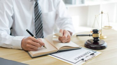 Hukuk danışmanlığı kavramı. Bir erkek savcı sözleşmesini kontrat kağıdına yazmadan önce kendi defteriyle gözden geçirir. 