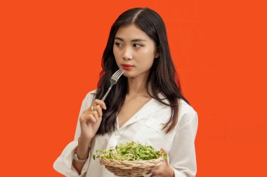 Vejetaryen konsepti, turuncu arka planda tek başına duran sağlıklı bir kadının ayçiçeği filizleri yemesi..