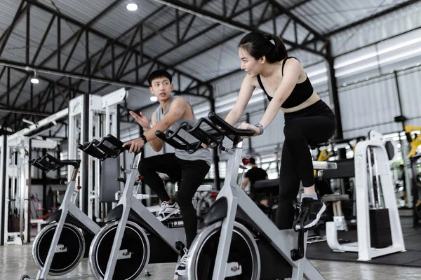 exercise concept The well-shaped lady and the muscular man being entertaining having small chat while riding the exercise bike machines.
