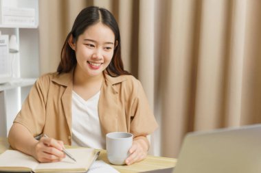 Çevrimiçi yaşam tarzı konsepti. Kadın ev işçisi not defterine kahve fincanı ile sunulan bilgileri yazıyor.