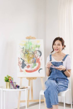 Sanat konsepti, genç Asyalı kadın boya fırçasını palete batırıp tuvale resim yapmak için kullanır..