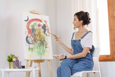 Sanat konsepti yaratıcısı, genç Asyalı kadın stüdyodaki sanat şaheserini boyamak için fırça kullanıyor..