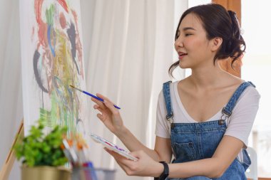 Sanat konsepti, genç Asyalı kadın resim çizmek için renk paletli boya fırçası kullanıyor..