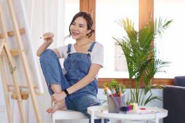 Sanat konsepti, genç Asyalı kadın resim yapmaya hazırlanmak için boya fırçası ve tuval tutuyor..