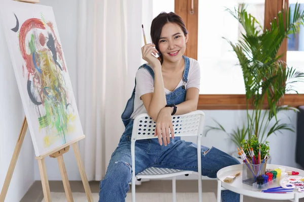 Sanat konsepti, genç Asyalı kadın boya fırçasını tutuyor ve bitirdikten sonra dinlenmek için oturuyor..