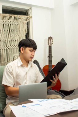 Uzaktan çalışma konsepti, erkek serbest yazar iş belgesini okur ve kanepe üzerinde çalışmak için dizüstü bilgisayar kullanır.