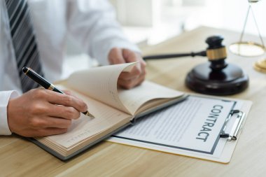 Hukuk danışmanlığı kavramı. Bir erkek savcı sözleşmesini kontrat kağıdına yazmadan önce kendi defteriyle gözden geçirir. 