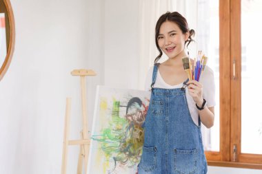 Sanat konsepti, resim çizdikten sonra elinde fırça ve resim tutan Asyalı genç bir kadın..