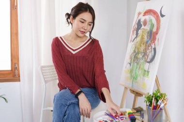 Sanat konsepti. Genç Asyalı kadın atölyede resim çizmek için boya fırçasını seçiyor..