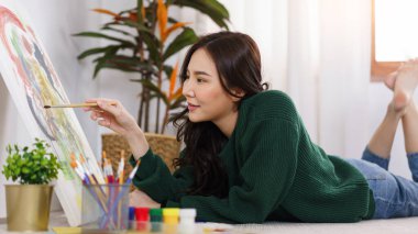 Sanat konsepti, genç Asyalı kadın yerde yatıyor ve resim yaparken boya fırçası kullanıyor..