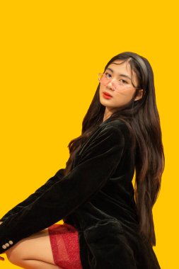 Moda konsepti, şık bir kadın elbise içinde poz vermek için oturuyor ve büyük boy siyah gözlüklü bir ceket giyiyor..