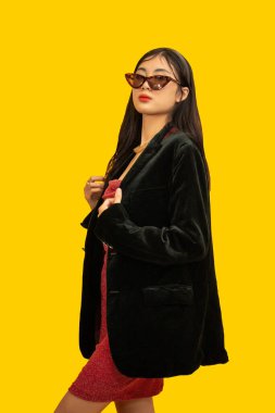 Moda konsepti. Moda kadını, büyük boy siyah ceketle poz vermek için güneş gözlüğü ve kırmızı elbise giyiyor..