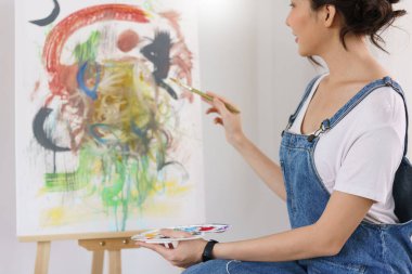 Sanat konsepti yaratıcısı, genç Asyalı kadın stüdyodaki sanat şaheserini boyamak için fırça kullanıyor..
