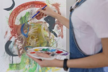 Sanat konsepti, genç Asyalı kadın resim çizmek için renk paletli boya fırçası kullanıyor..