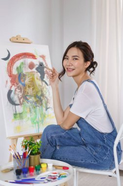 Sanat konsepti, resim çizerken elinde fırça tutan ve gülümseyen Asyalı genç kadın..
