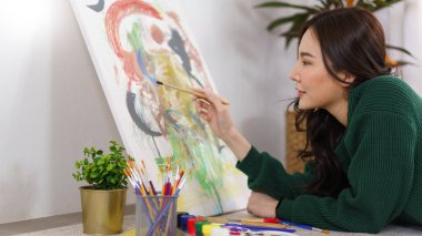 Sanat konsepti, genç Asyalı kadın yerde yatıyor ve resim yaparken boya fırçası kullanıyor..