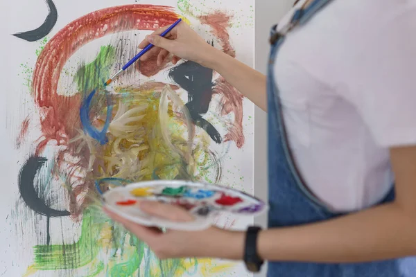 Sanat konsepti, genç Asyalı kadın resim çizmek için renk paletli boya fırçası kullanıyor..
