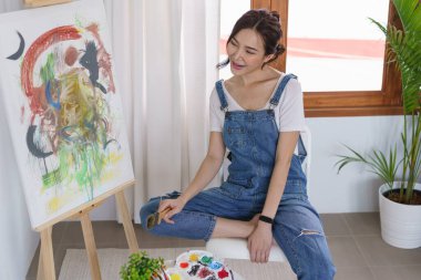 Sanat konsepti, genç Asyalı kadın boya fırçası tutuyor ve sanat şaheserine bakmaktan mutlu..