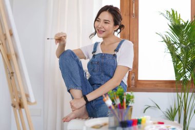 Sanat konsepti, genç Asyalı kadın resim yapmaya hazırlanmak için boya fırçası ve tuval tutuyor..