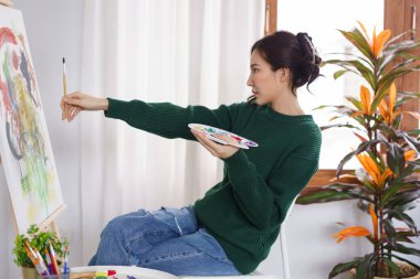 Sanat konsepti, genç Asyalı kadın boy ölçümü için boya fırçasını tuvalin önünde tutuyor..