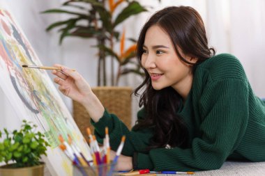 Sanat konsepti, genç Asyalı kadın yerde yatıyor ve resim yaparken boya fırçası kullanıyor..