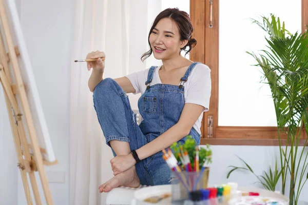 Sanat konsepti, genç Asyalı kadın resim yapmaya hazırlanmak için boya fırçası ve tuval tutuyor..