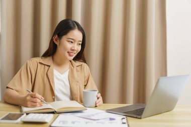 Çevrimiçi yaşam tarzı konsepti. Kadın ev işçisi not defterine kahve fincanı ile sunulan bilgileri yazıyor.