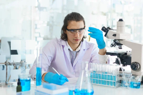 Laboratuvar araştırma konsepti, bilim adamı test tüpündeki numuneyi analiz ediyor ve deney sonuçlarını yazıyor..