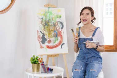 Sanat konsepti, genç Asyalı kadın boya fırçası tutuyor ve tuvalde resim yapmaya çalışıyor..