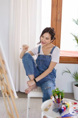 Sanat konsepti, genç Asyalı kadın resim yapmaya hazırlanmak için boya fırçası ve tuval tutuyor..